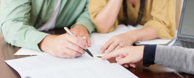 man and a woman pointing at documents holding a pen with someone pointing to the paper prenuptial and mid marriage agreements