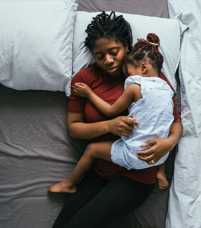 african american woman holding her young daughter in bed