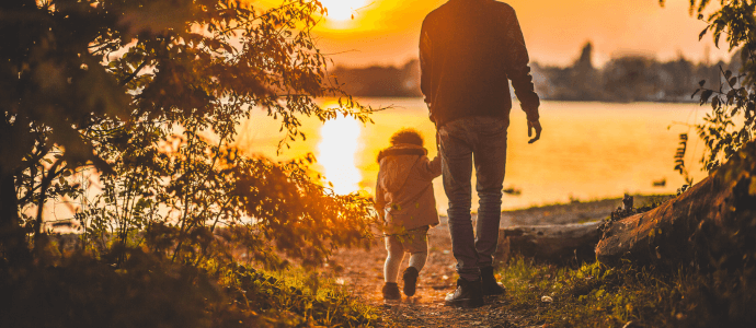 father walking with child near a lake during a sunset