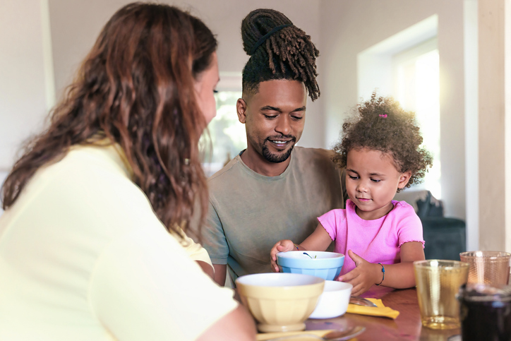 A heartwarming scene of a Caucasian mother, African father, and their daughter enjoying breakfast together in the living room, showcasing the beauty of multicultural family moments.