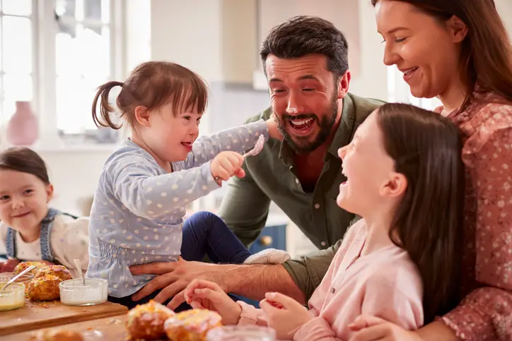 Family With Down Syndrome Daughter Baking And Decorating Cakes Sitting Around Table At Home